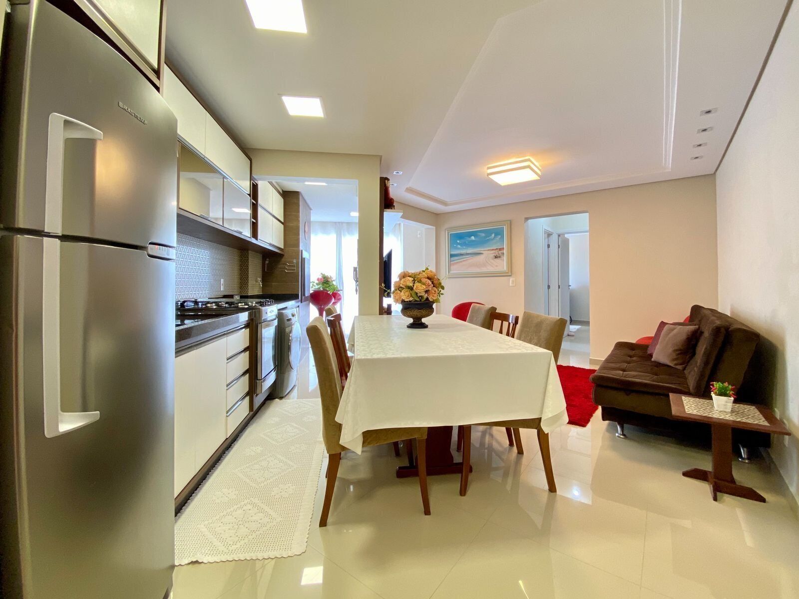 Une cuisine moderne équipée d’appareils électroménagers en acier inoxydable, un coin repas avec une table et des chaises, et un salon avec un canapé et une petite table d’appoint.