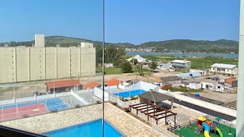 Vista de uma piscina, área de recreação infantil e quadra esportiva vista da janela.