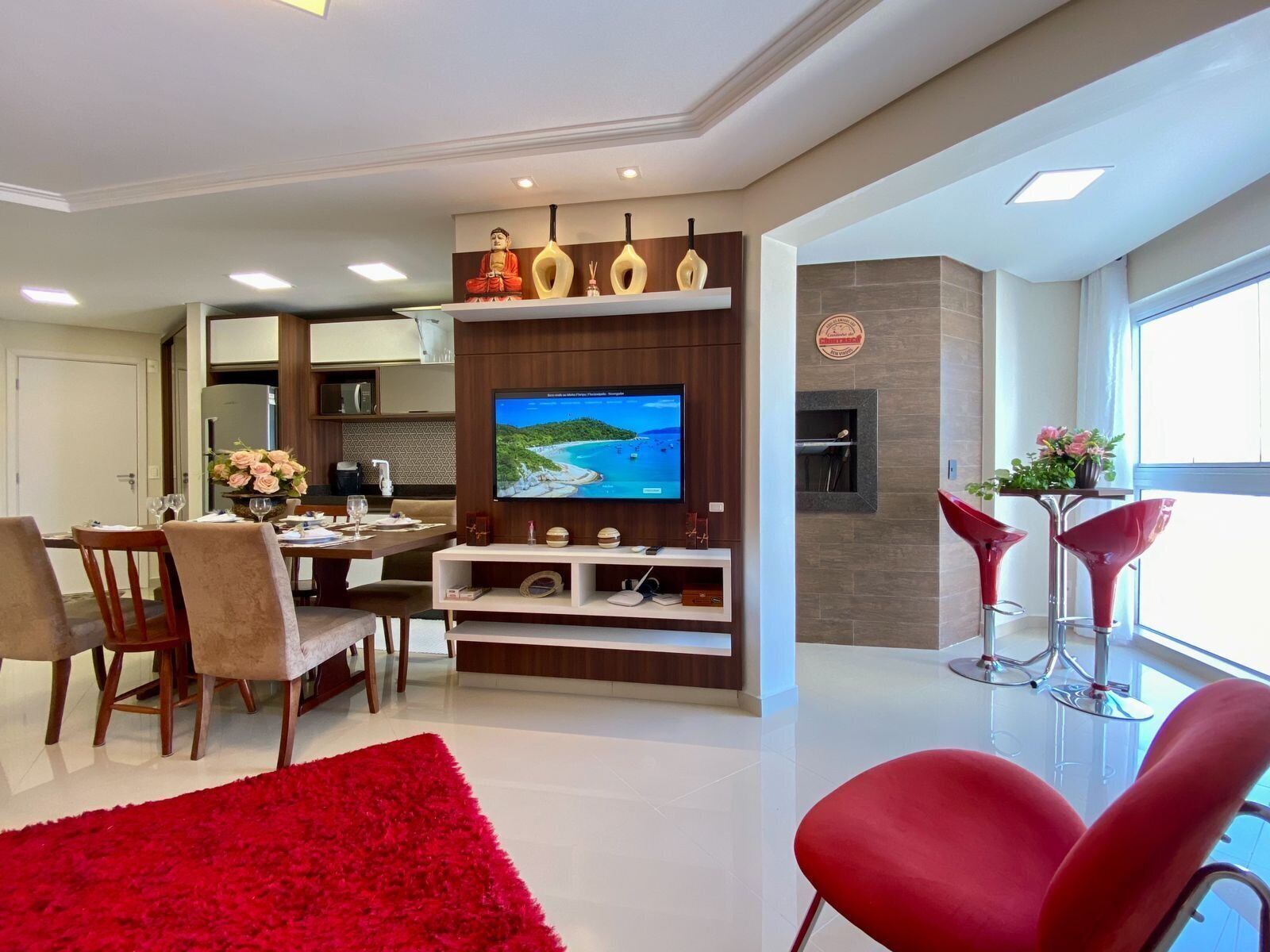Uma sala de estar moderna com televisão, área de jantar e cadeiras vermelhas.