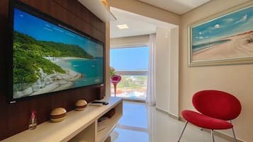 Un salon moderne avec un grand téléviseur à écran plat posé sur un meuble bas en bois, un fauteuil rouge et un tableau représentant une scène de plage accroché au mur.