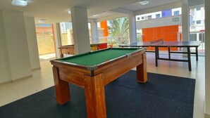 Une table de billard dans un espace intérieur bien éclairé, doté de grandes fenêtres et offrant une vue sur l’extérieur.