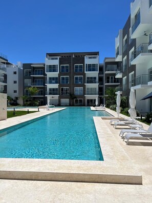 Ein Schwimmbecken mit Liegestühlen und Sonnenschirmen, umgeben von modernen Apartmentgebäuden.