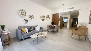 A modern living room with a grey sofa, a coffee table, and a dining area with chairs. - Hard Rock Punta Cana Coral Bay II (Punta Cana)