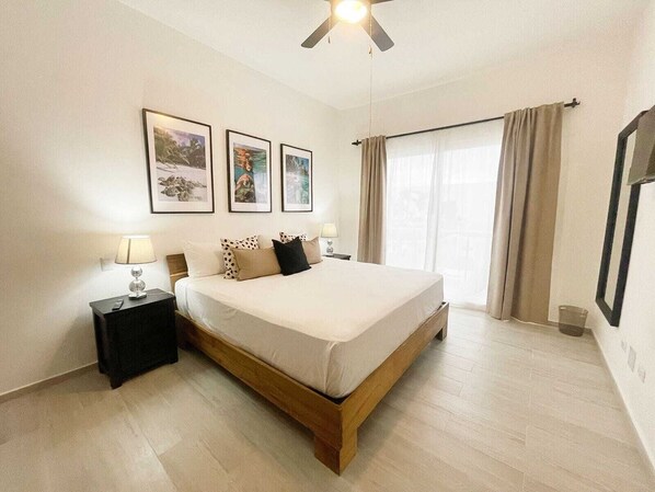 A bedroom with a bed, two bedside tables, a ceiling fan, and a window with curtains. - Hard Rock Punta Cana Coral Bay II (Punta Cana)
