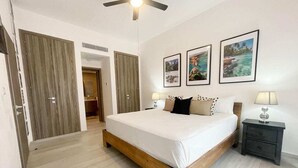 A bedroom with a wooden bed, two bedside tables with lamps, a ceiling fan, and framed pictures on the wall. - Hard Rock Punta Cana Coral Bay II (Punta Cana)