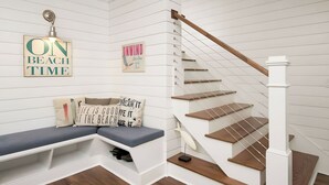 A staircase with wooden steps and a white railing, a bench with cushions, and wall decorations including a sign that says 'ON BEACH TIME'. - 3405 Cameron by Avantstay Pool, Outdoor Kitchen (Isle of Palms)