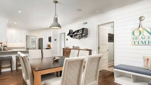 A modern kitchen with white cabinetry, a wooden dining table, and a built-in bookshelf. - 3405 Cameron by Avantstay Pool, Outdoor Kitchen (Isle of Palms)