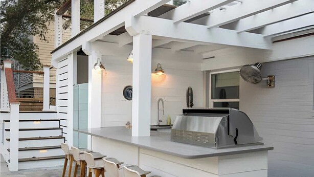 An outdoor kitchen with a grill, bar stools, and pendant lights. - 3405 Cameron by Avantstay Pool, Outdoor Kitchen (Isle of Palms)