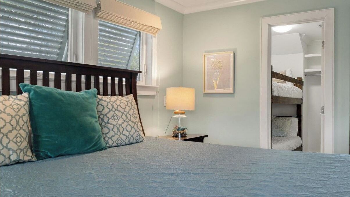 A bedroom with a bed, pillows, a nightstand, a lamp, a framed picture, and a closet.