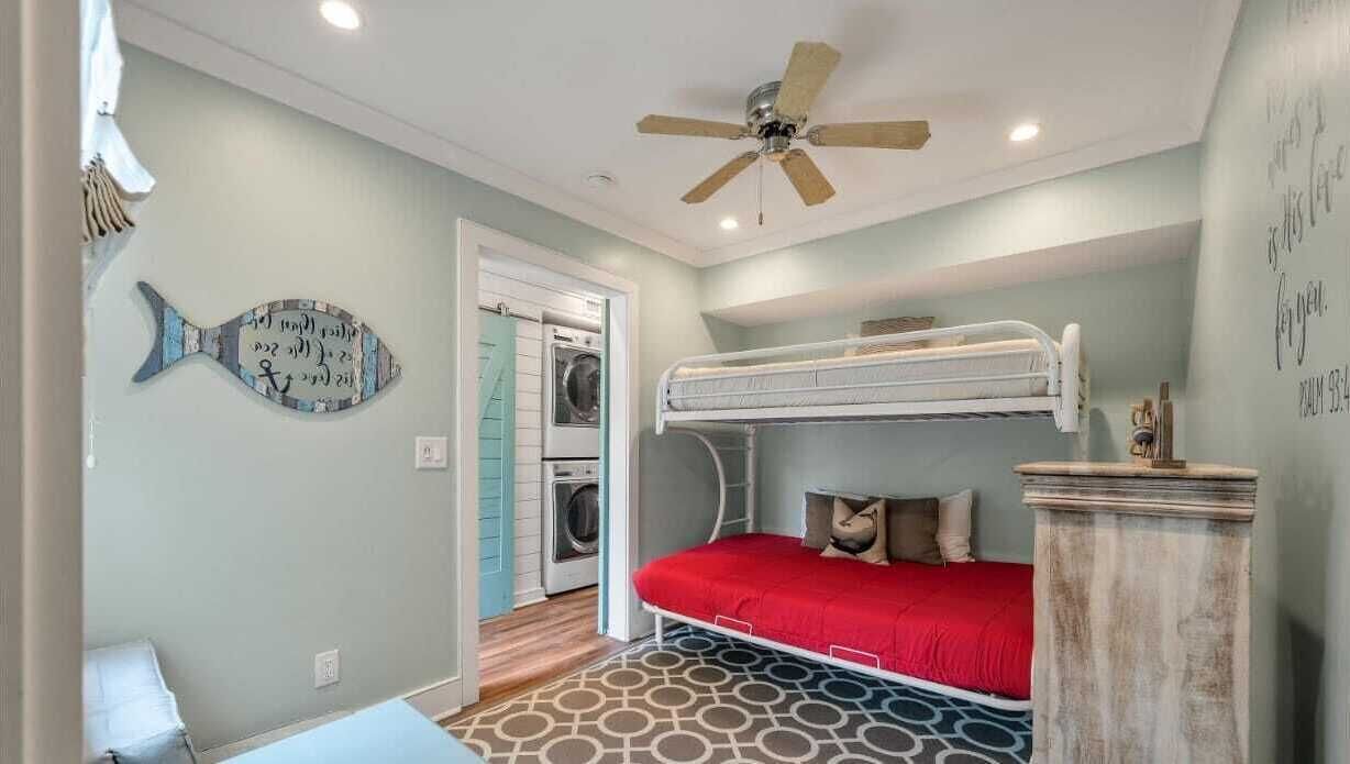 Une chambre compacte avec un lit superposé, un ventilateur de plafond, un élément de décoration murale en forme de poisson et un lave-linge dans la pièce adjacente.