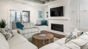 A modern living room with a fireplace, white sofas, a round coffee table, and a TV mounted on the wall. - 3405 Cameron by Avantstay Pool, Outdoor Kitchen (Isle of Palms)