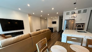 A modern living room with a sofa, a dining table with placemats, and a kitchen area with cabinets and a refrigerator.