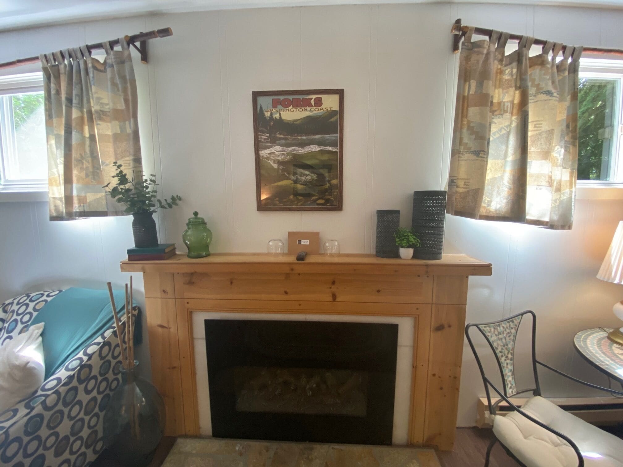 A living room with a fireplace, a framed poster on the wall, and a window with curtains.