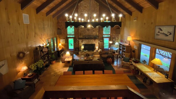 A cozy lodge interior with a high ceiling, wooden beams, a fireplace, and a dining area. - Manitou Lodge (Forks)