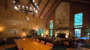 A spacious living room with a large wooden dining table, comfortable seating, a stone fireplace, and a stone wall. - Manitou Lodge (Forks)