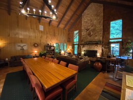 Amplia sala de estar con una gran mesa de comedor de madera, asientos cómodos, chimenea de piedra y una pared de piedra.