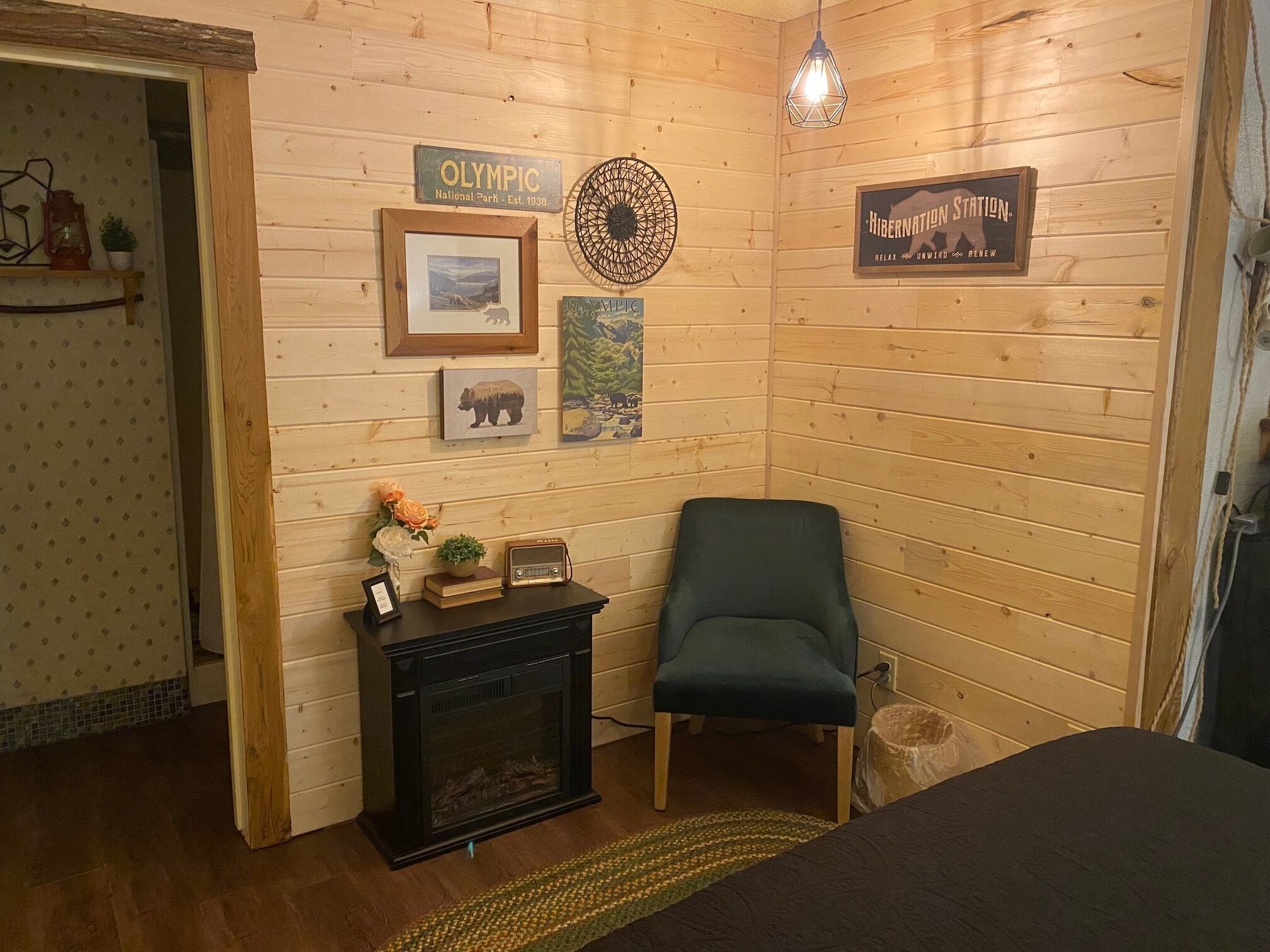 Una habitación acogedora con paredes de madera, chimenea, una silla y varios cuadros y letreros enmarcados.