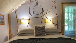 A bedroom with a bed, two wall-mounted lamps, a dreamcatcher, and a door with blinds. - Manitou Lodge (Forks)