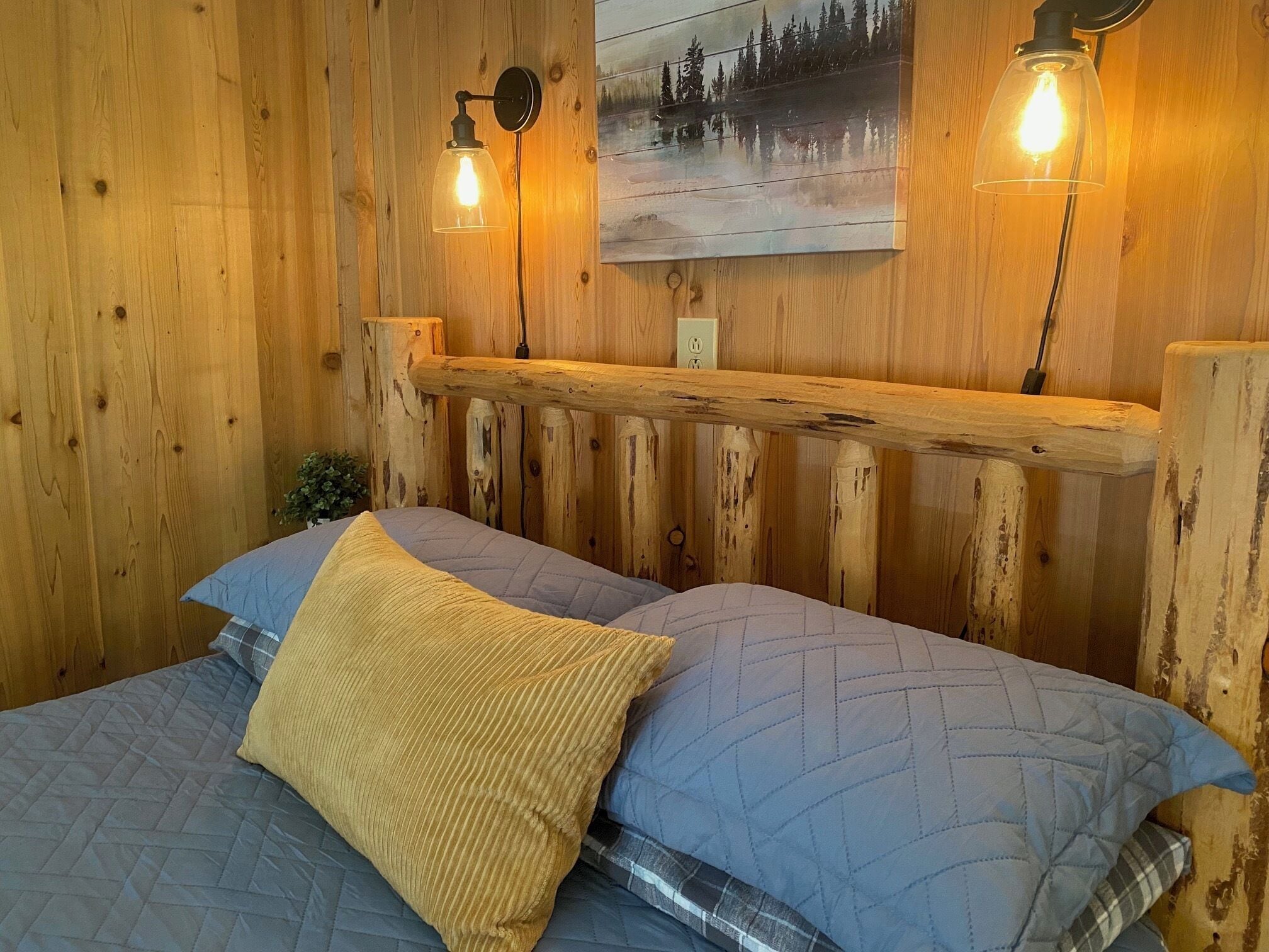 Habitación tipo cabaña de madera con dos camas, cabeceros de madera y dos lámparas de pared.