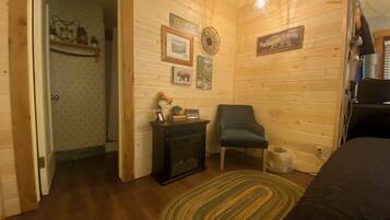 Ein gemütliches Zimmer mit Holzwänden, einem grünen Sessel, einem kleinen Tisch mit einem Radio und einem Schild mit der Aufschrift 'Hibernation Station'.
