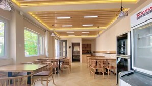 A restaurant with wooden tables and chairs, a kitchen area, and a large window providing natural light. - Changdao Shuanglin Homestay (Yantai)