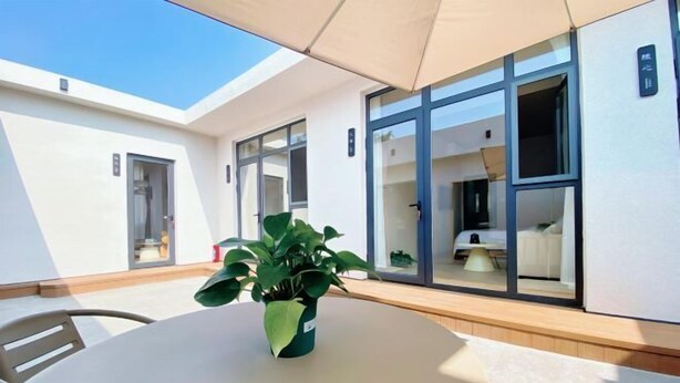 A modern hotel room with large sliding glass doors, a round table with a potted plant, and a visible bathroom. - Changdao Shuanglin Homestay (Yantai)