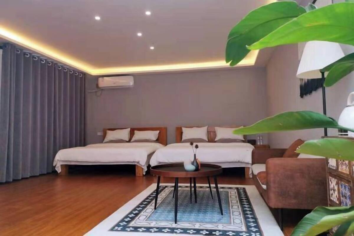 A hotel room with two beds, a round coffee table, a sofa, and a large plant.