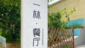 A sign for Yilin Restaurant with Chinese characters, a wooden fence, and greenery in the background. - Changdao Shuanglin Homestay (Yantai)