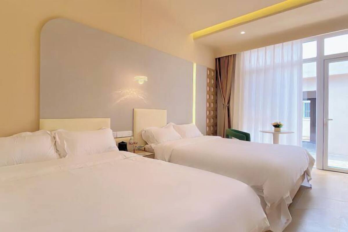 A hotel room with two beds, a small table, and a view of the outdoors.