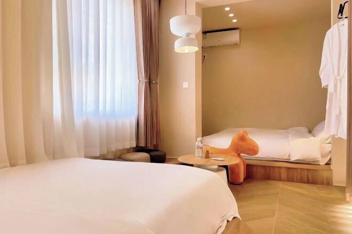 A hotel room with a bed, a small table, a chair, a nightstand, and a window with curtains.