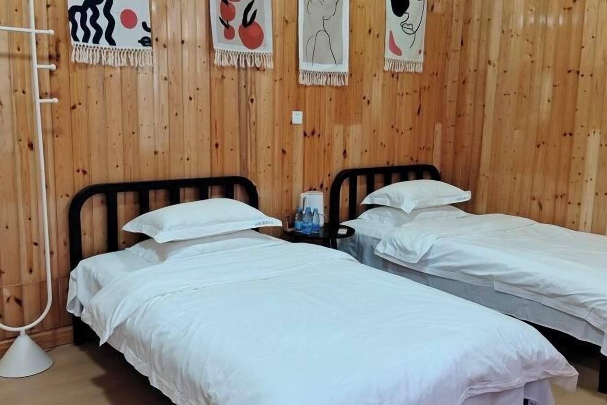 A room with two single beds, wooden panel walls, and a small table with a water bottle.
