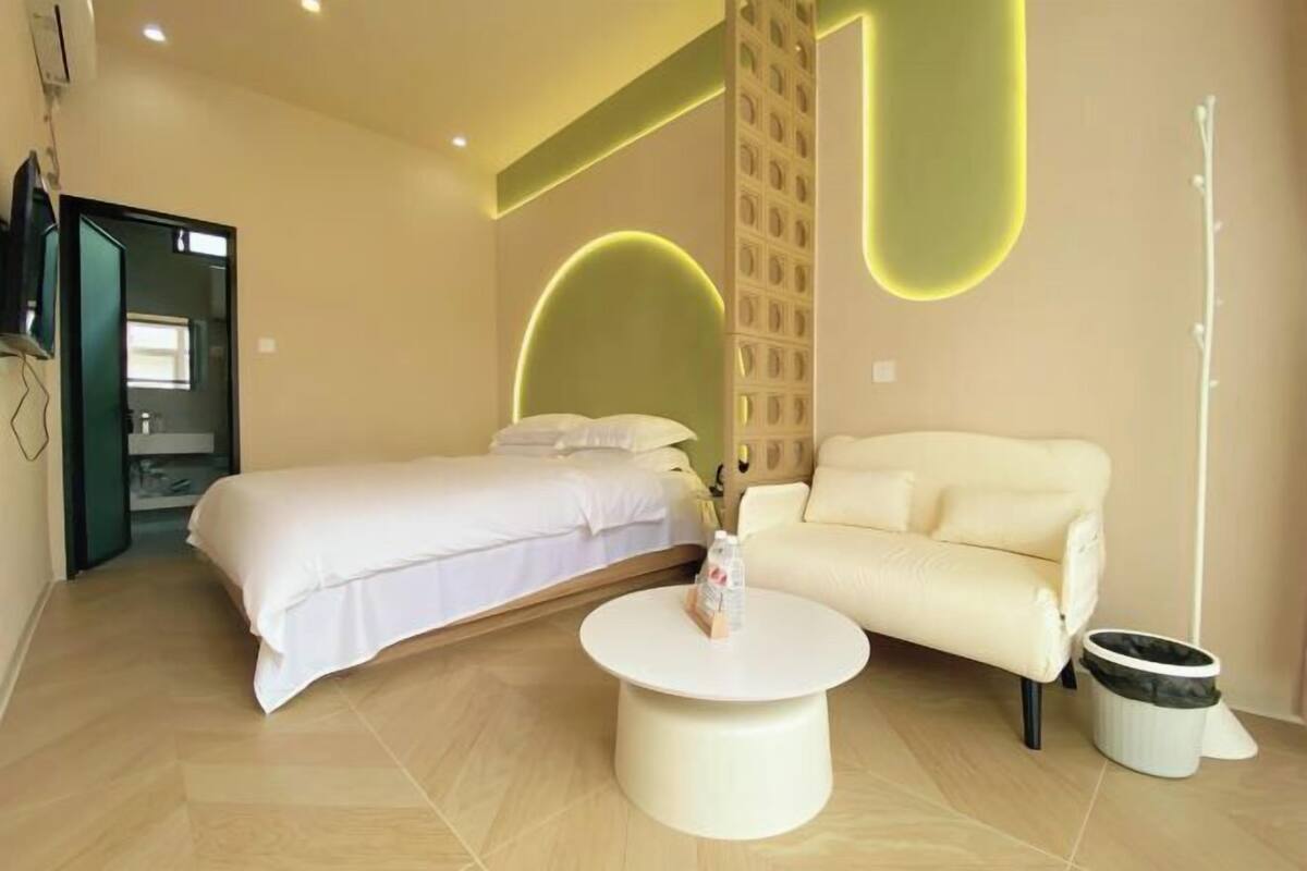 A hotel room with a bed, a sofa, a round coffee table, and a trash bin.