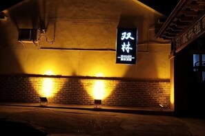 Un bâtiment à la façade en briques, une enseigne avec des caractères chinois et deux lampes illuminées au sol.