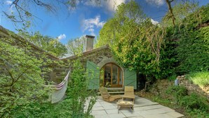 Ein Steinhaus mit einer Holztür, einer Hängematte und einer Terrasse mit zwei Holzstühlen.