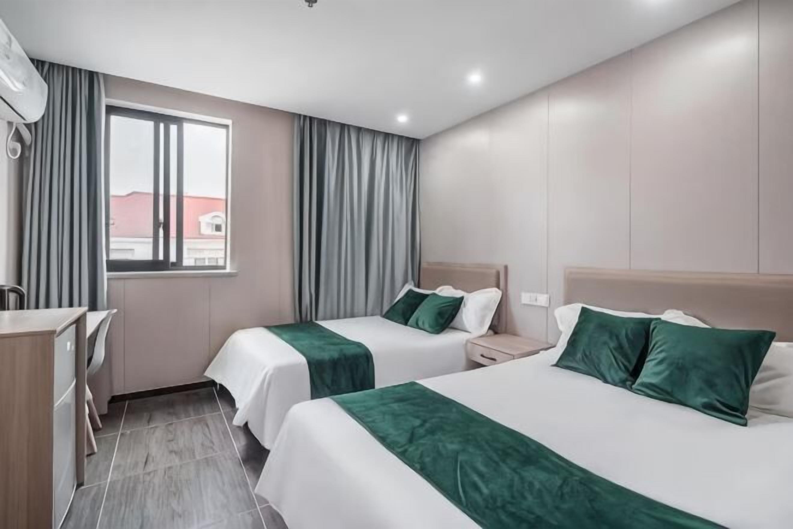 A hotel room with two beds, a desk, and a window with curtains.