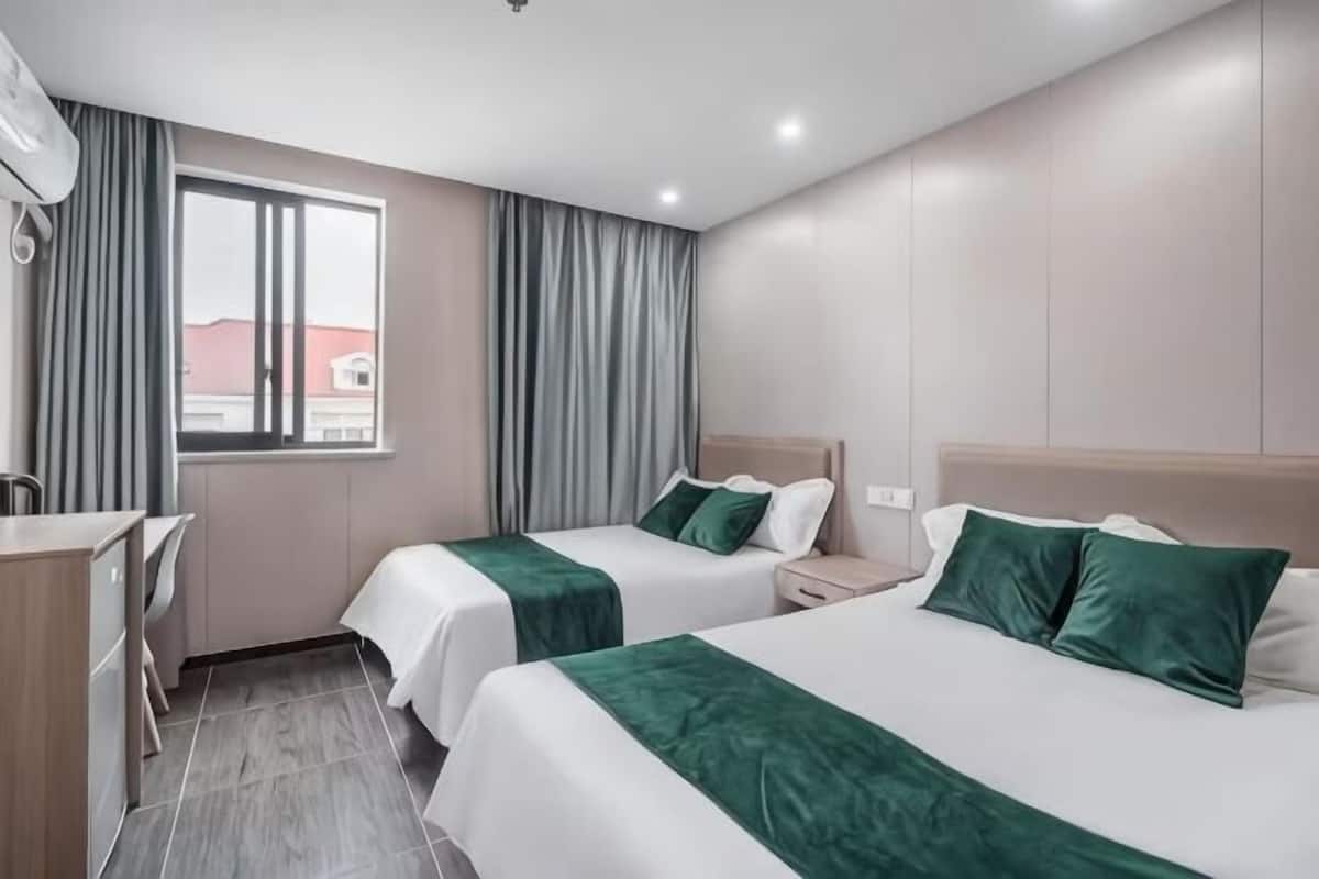 A hotel room with two beds, a desk, and a window with curtains.