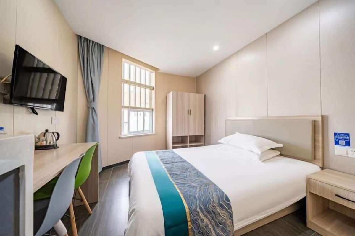 A hotel room with a bed, a desk, a chair, a television, a wardrobe, and a window.
