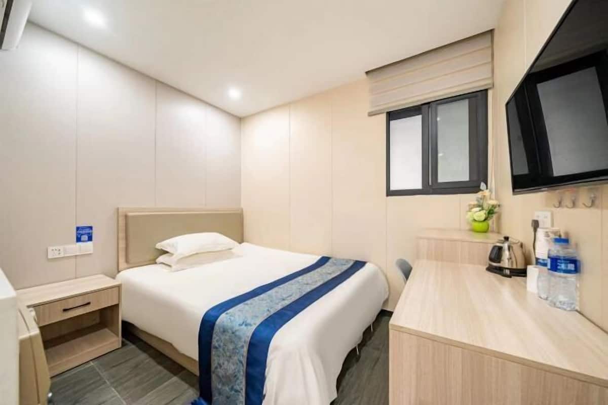 A hotel room with a bed, a desk, a window, and a TV.