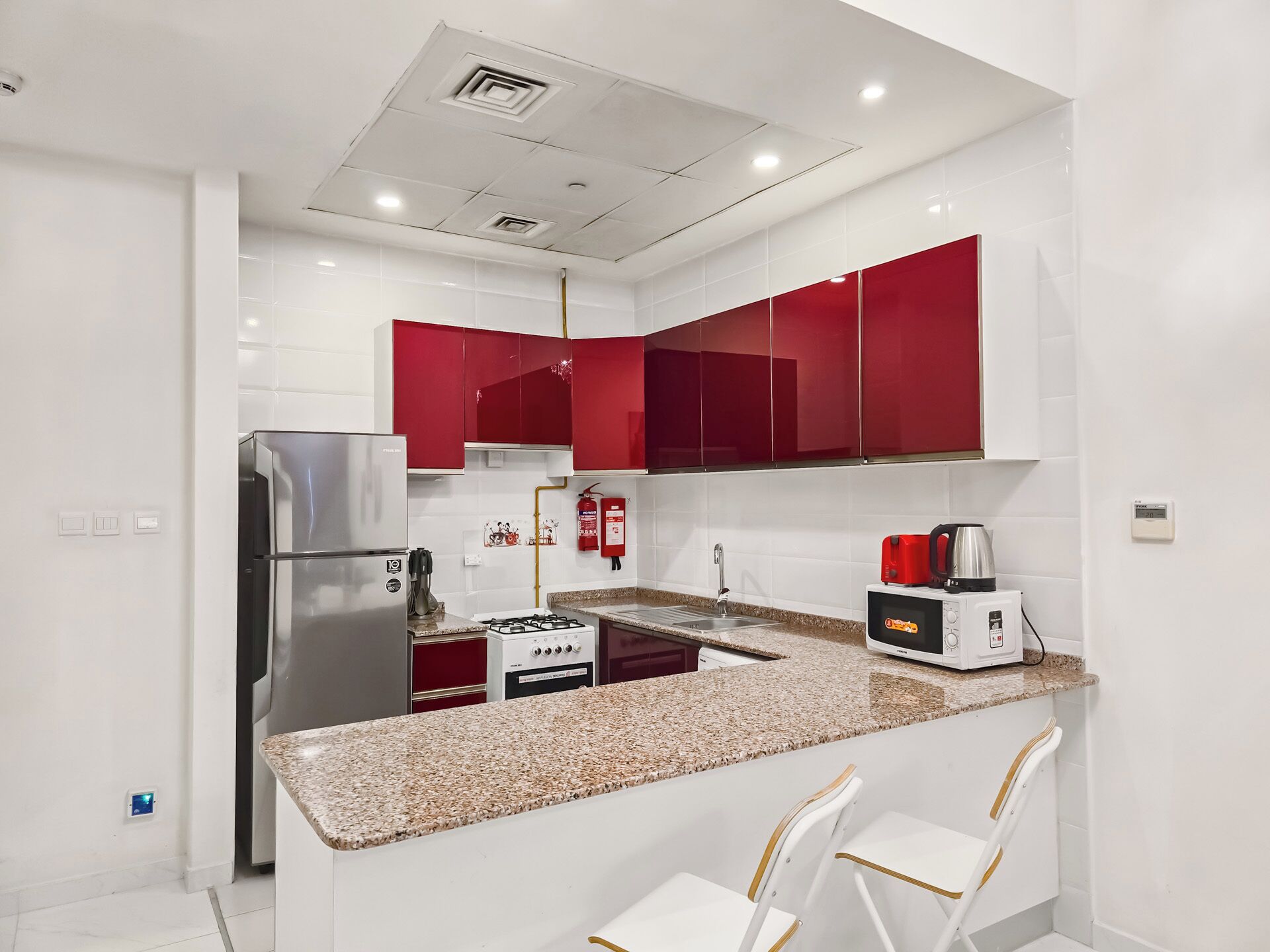 A modern kitchen with white and red cabinetry, stainless steel appliances, and a granite countertop.