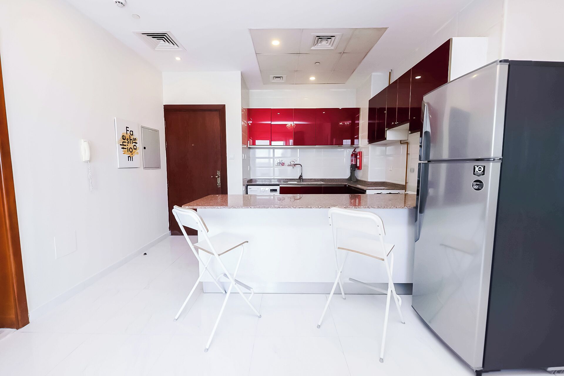 Une cuisine moderne avec des meubles blancs, un réfrigérateur en acier inoxydable et deux chaises blanches.