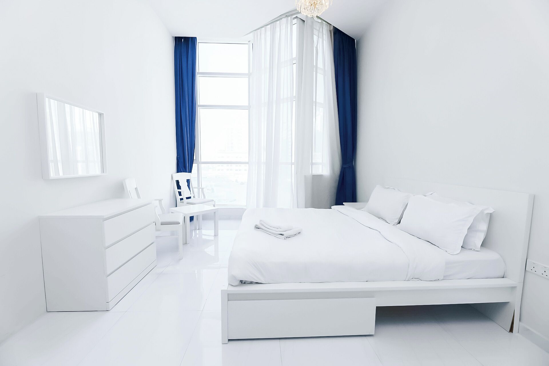 A modern, white-themed bedroom with a bed, dresser, and chair.