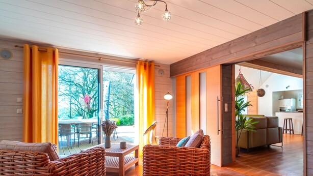 A modern living room with wicker furniture, a dining area, and a view of the outdoors. - Le Chêne Sacré - Piscine intérieur (Plouay)