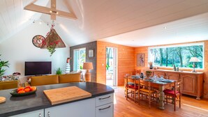 A modern kitchen with a wooden dining area, a large window, and a TV. - Le Chêne Sacré - Piscine intérieur (Plouay)