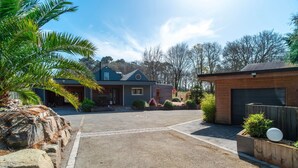 A residential property with a driveway leading to a house, a garage, and a landscaped garden with a palm tree and rocks. - Le Chêne Sacré - Piscine intérieur (Plouay)