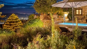 Un espacio exterior nocturno con piscina, sillones de descanso y una sombrilla grande.