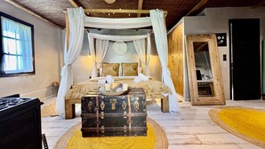 Un dormitorio con cama con dosel, un cofre de madera y un ventilador de techo.