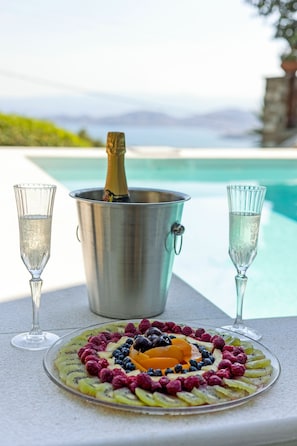 Ett bord med ett fat med frukt, två champagneglas och en champagnekylare vid poolkanten.