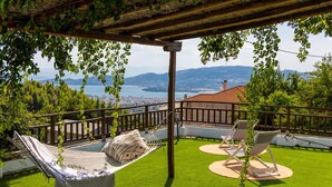 Una terraza con una hamaca, dos sillones de descanso y vistas a un lago y montañas.