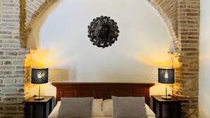 Ein Schlafzimmer mit einem Ziegelbogen, einem hölzernen Kopfteil, zwei Nachttischen mit Lampen und zwei Kissen mit Muster.