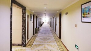 A long hallway with a patterned carpet, doors on both sides, and a light-colored wall with a framed picture.